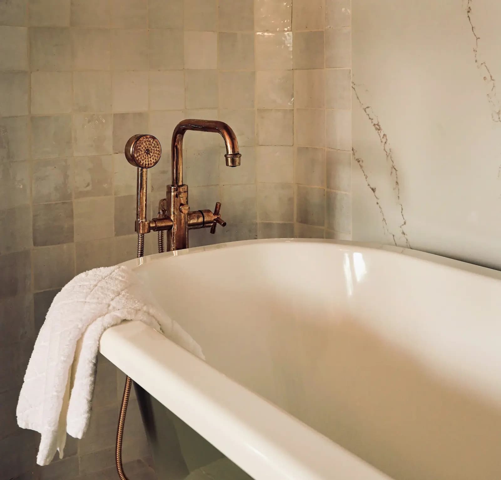 Freestanding bath with a copper floor-mounted mixer and hand shower against handmade tiles